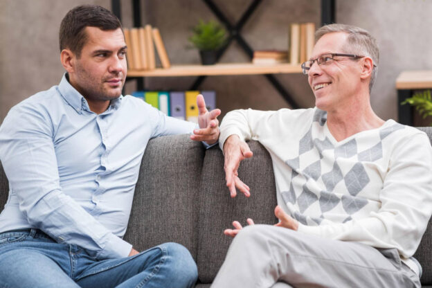 Two men sit on a couch engaged in a thoughtful conversation, suggesting guidance and support during treatment decision-making.
